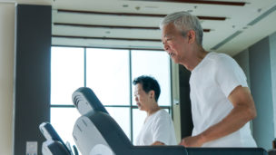 Old healthy Asian senior couple exercise together in gym running treadmill