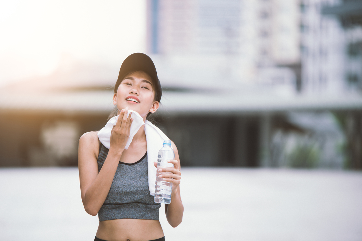 Wiping sweat Thirsty female jogger drinking fresh water after training. Young athletic woman exercising in the city park outdoors.
