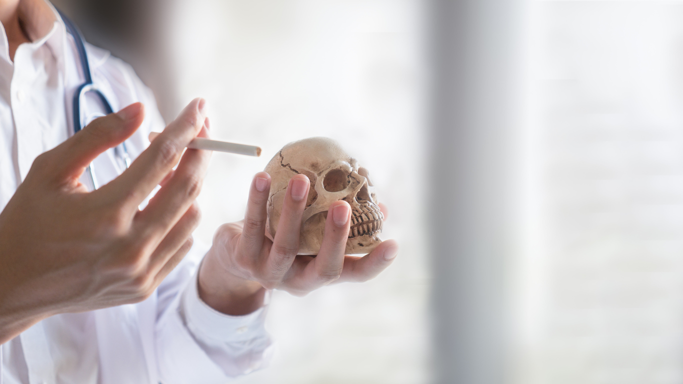 The medical doctor with stethoscope hold skull in one hand and cigarette in one hand in the concept of the danger of smoking and stop smoking, Closeup and soft tone