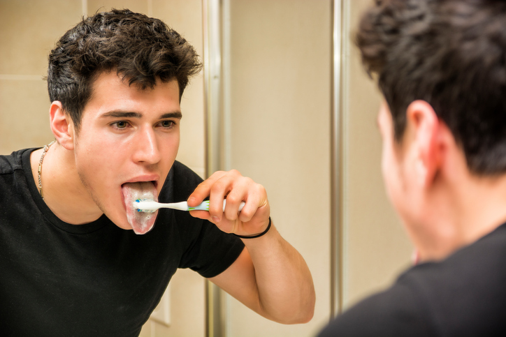 Headshot of attractive young man brushing teeth and tongue