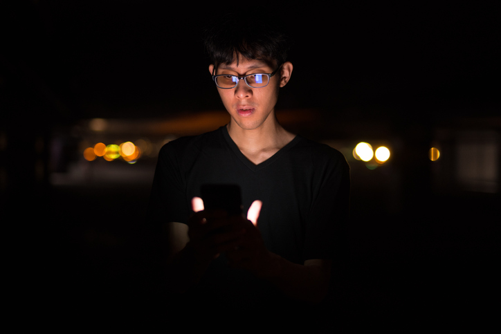 Portrait Of Asian Man Outdoors At Night In Parking Lot Using Mobile Phone
