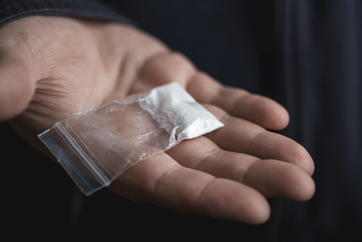 Mans hand holding on palm plastic packet with cocaine powder or another drugs. Drug dealer proposes to try narcotic concept