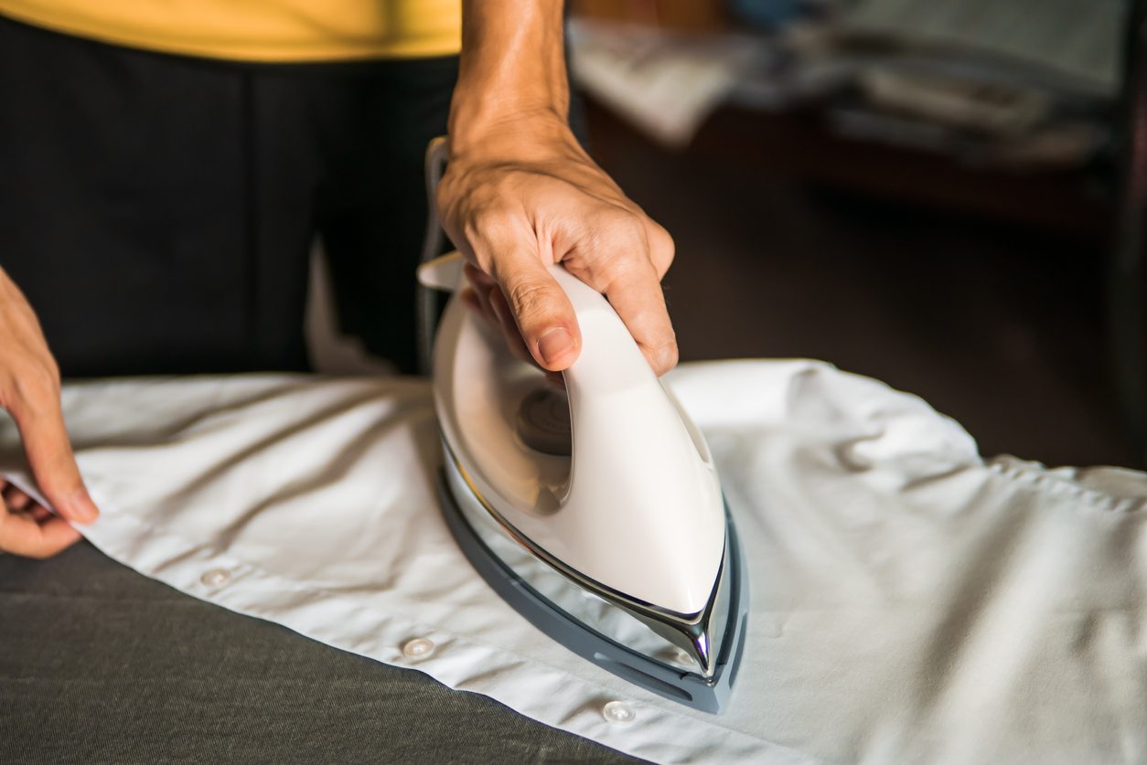 Men hand ironing white shirt on ironing board
