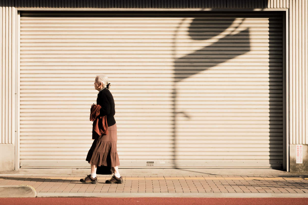 Aging population social issue of a widow lonely woman walking along the street of Japan