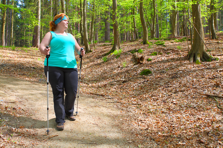 Overweight woman walking on forest trail. Slimming and active lifestyle theme.