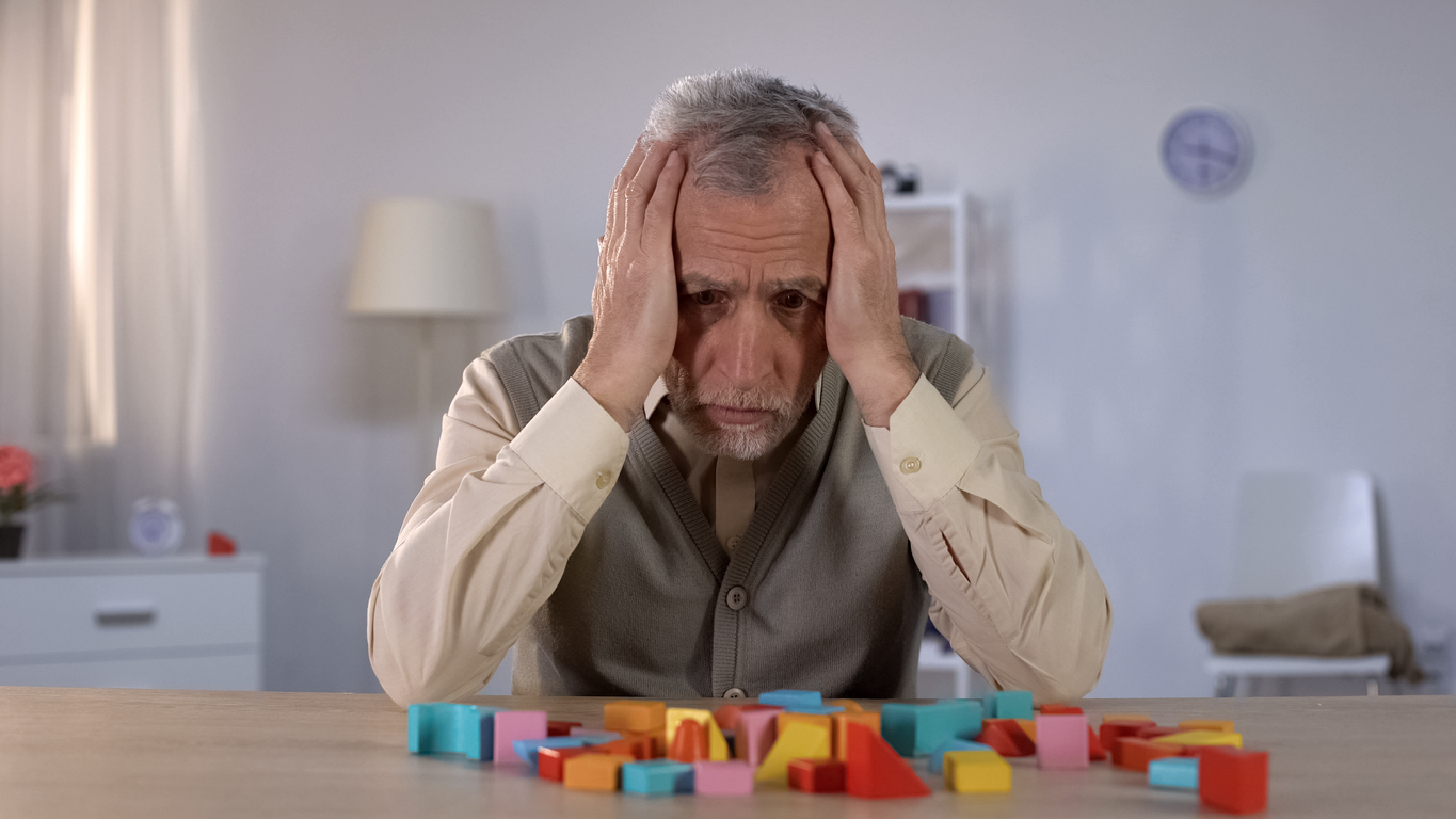 Pensive elderly man looking at color building blocks on table, old age dementia