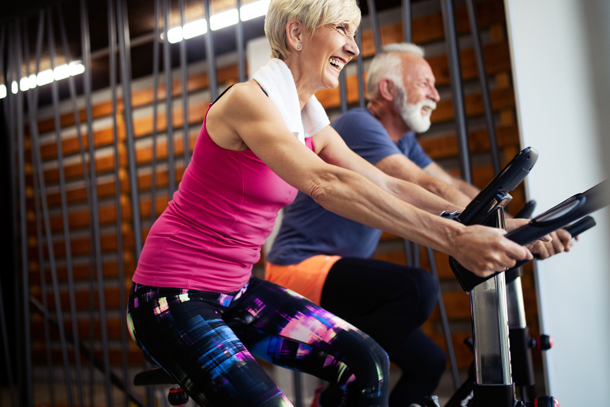 Mature fit people biking in the gym, exercising legs doing cardio workout cycling bikes