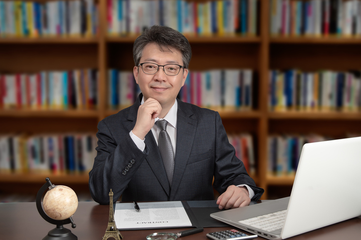 A portrait of an Asian middle-aged male businessman sitting at a desk.