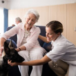 Portrait of smiling female doctor kneeling by senior woman stroking puppy