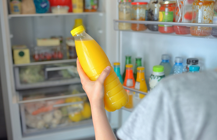 Teenage girl takes the orange juice from the open refrigerator