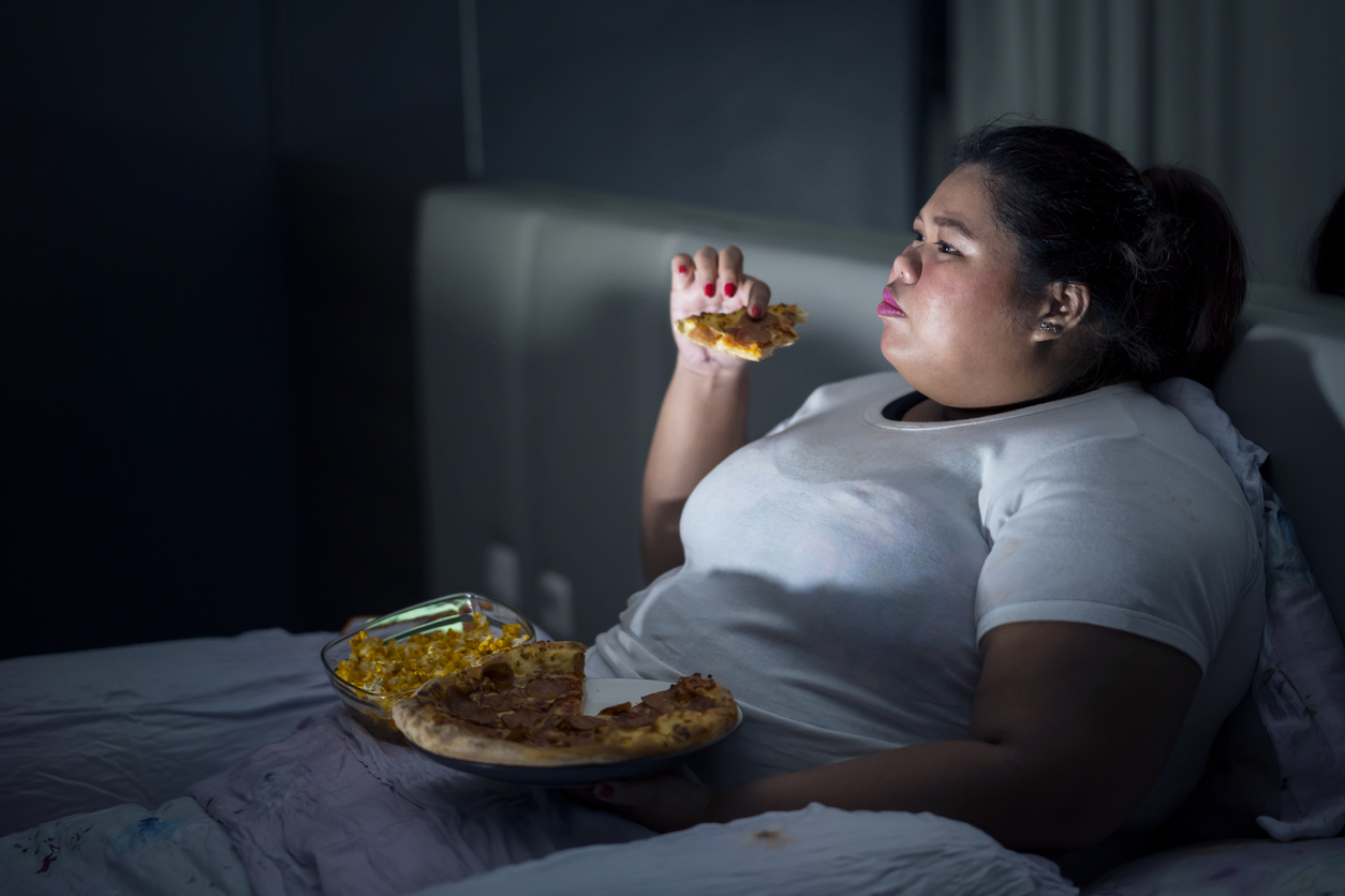 Fat woman eating pizza on bed