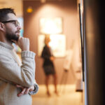 Bearded Man Looking at Paintings in Art Gallery
