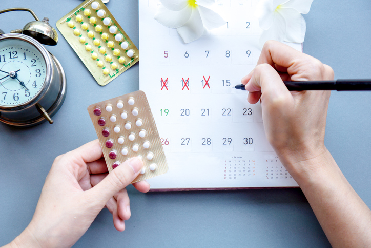 woman hand holding contraceptive pills and mark the date on calendar