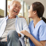 friendly asian caretaker talking to senior patient in nursing home