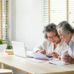 Stressed Asian Senior Couple using calculator and calculate family budget, Debts, monthly expenses in home during Financial economic crisis. Senior man and woman looking at account book, bill, passbook, receipt and laptop computer on table
