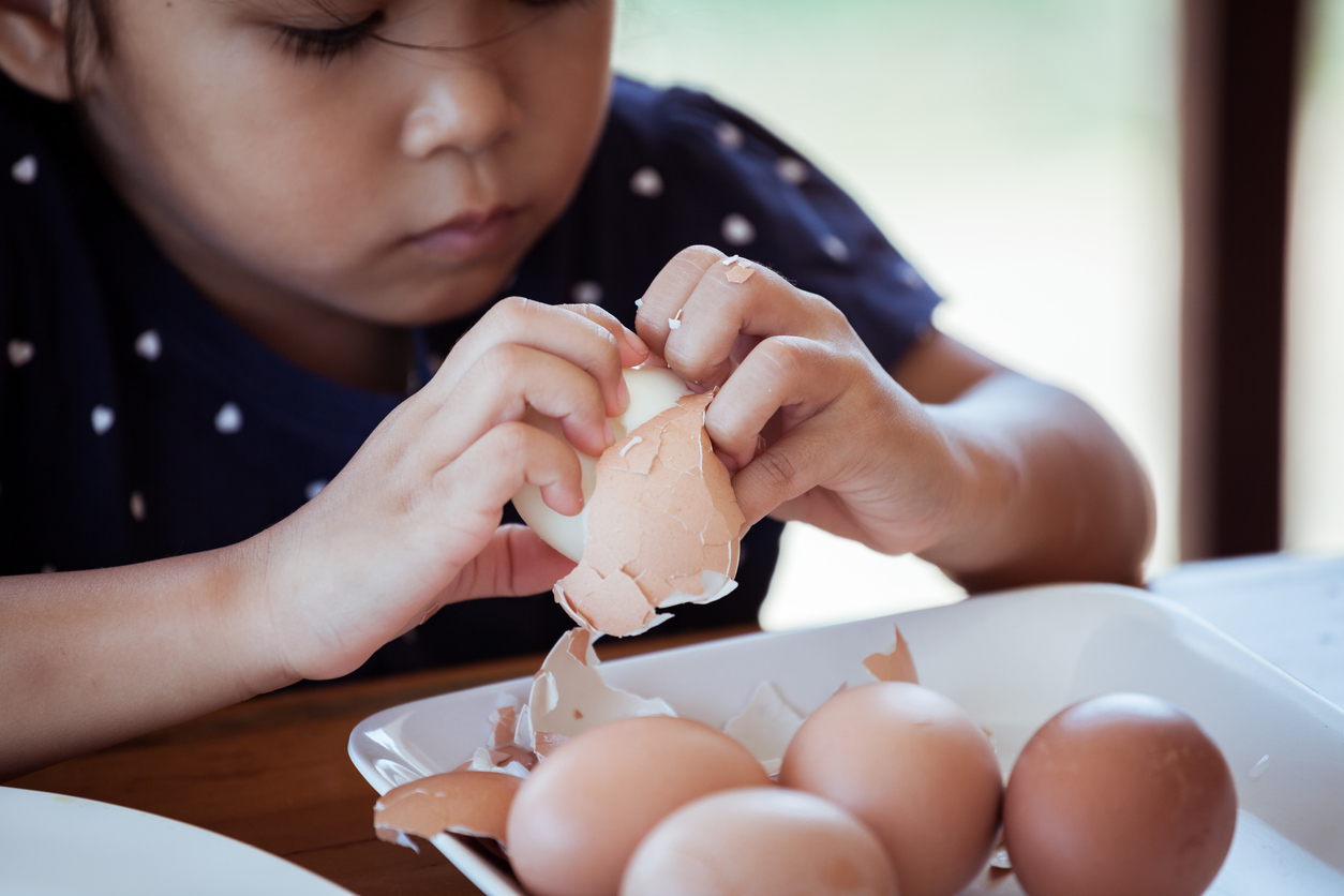 Asian little girl helping mother to peel egg