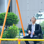 Middle aged asian businessman riding on swing.