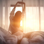 Happy woman stretching in bed after waking up. Happy young girl greets good day.